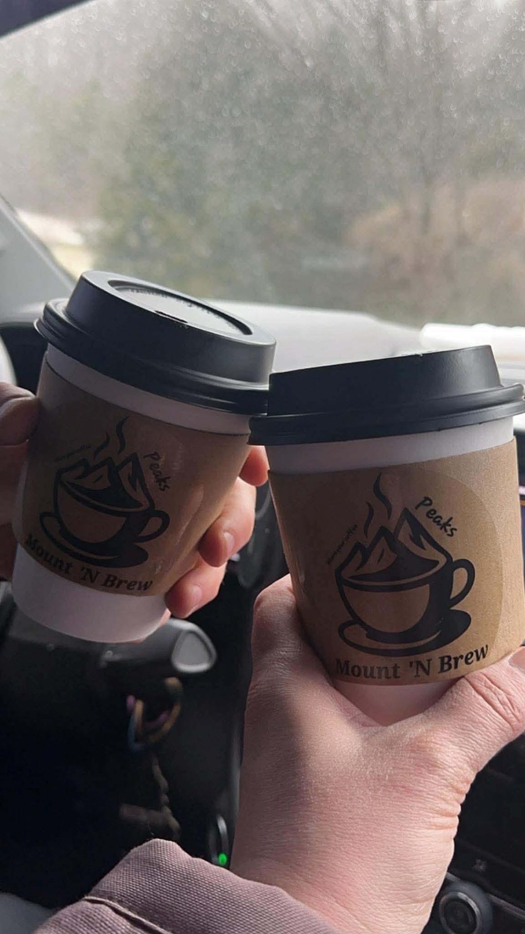Two Mount 'N Brew branded hot coffees toasted together in the car.